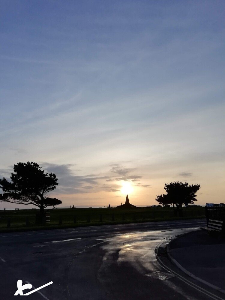 雨を浴びた石碑に差す夕陽。ヘイロー(後光)の如く人道をも照らす。