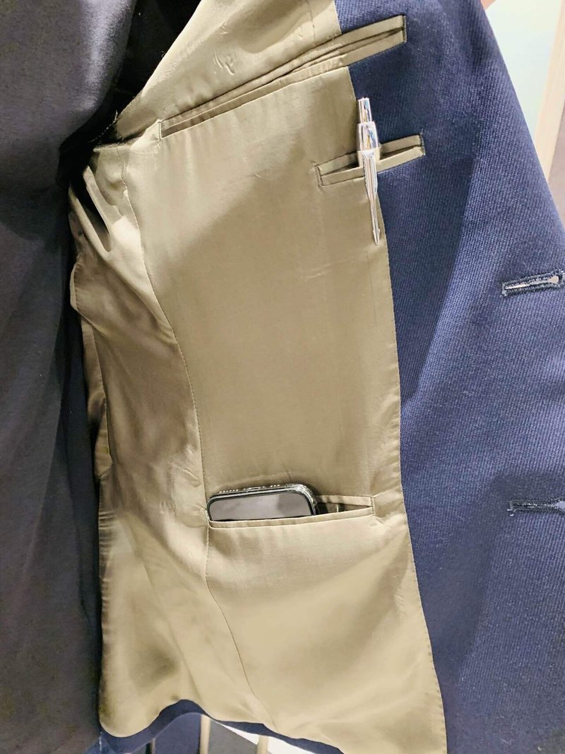 FABRIC TOKYOのスーツのジャケット。青寄りのネイビーの表地（左身頃）をめくって、ベージュの裏地を見せている。ポケットが胸の辺りに一つ、その下にペンが入る細長いポケットが一つ、腰の辺りにもう一つポケットが見える。ペンやスマートフォンがしっかり入る。