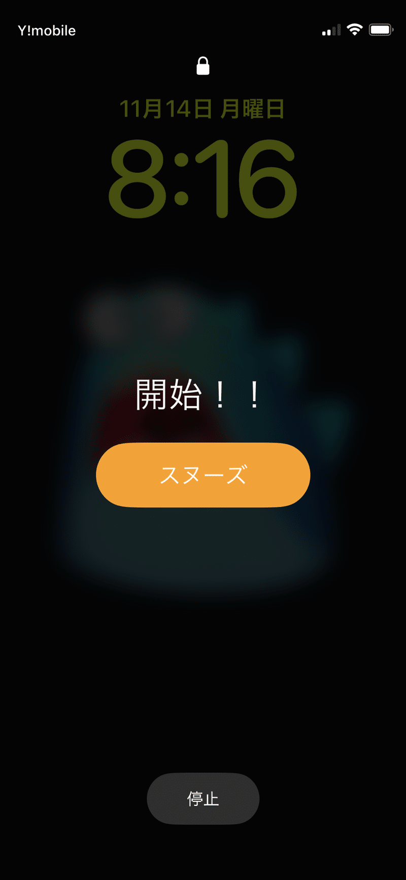 iPhoneのアラームが作動しているところ。画面には開始!!とかかれている。画面上部には鍵のアイコンが表示されている。(ロックが解除されていない状態)