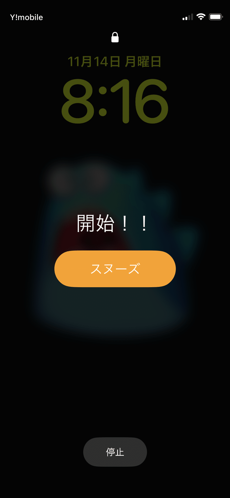 iPhoneのアラームが作動しているところ。画面には開始！！とかかれている。画面上部には鍵のアイコンが表示されている。（ロックが解除されていない状態）